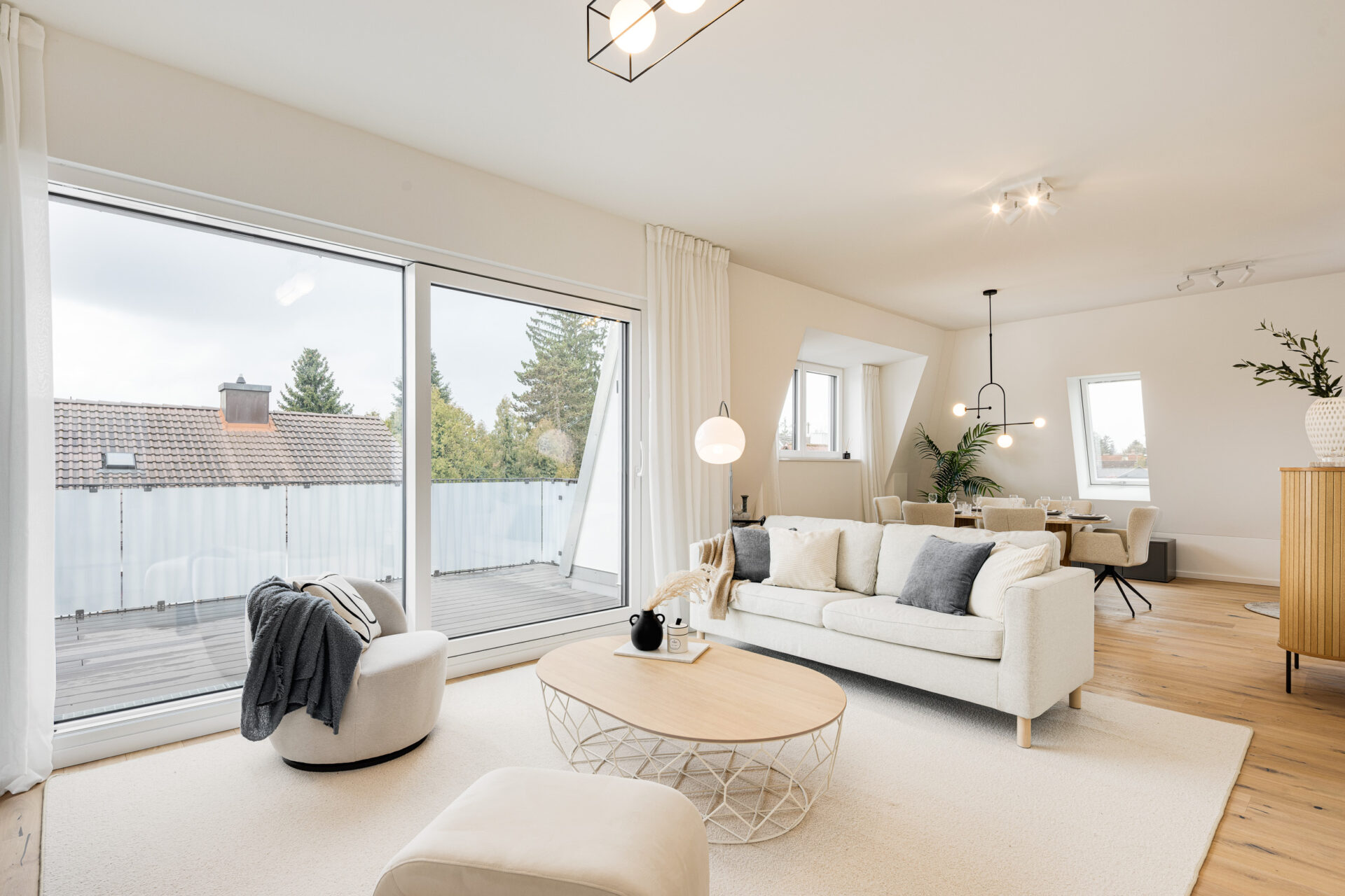 Foto eines Wohnzimmers mit Sofa und Esstisch im Dachgeschoss einer bezugsfertigen Neubauwohnung in Trudering von Domino Bau, mit Blick auf die Loggia